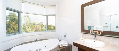 A modern bathroom with a large bathtub, a vanity with a mirror, and a window offering a view of trees.