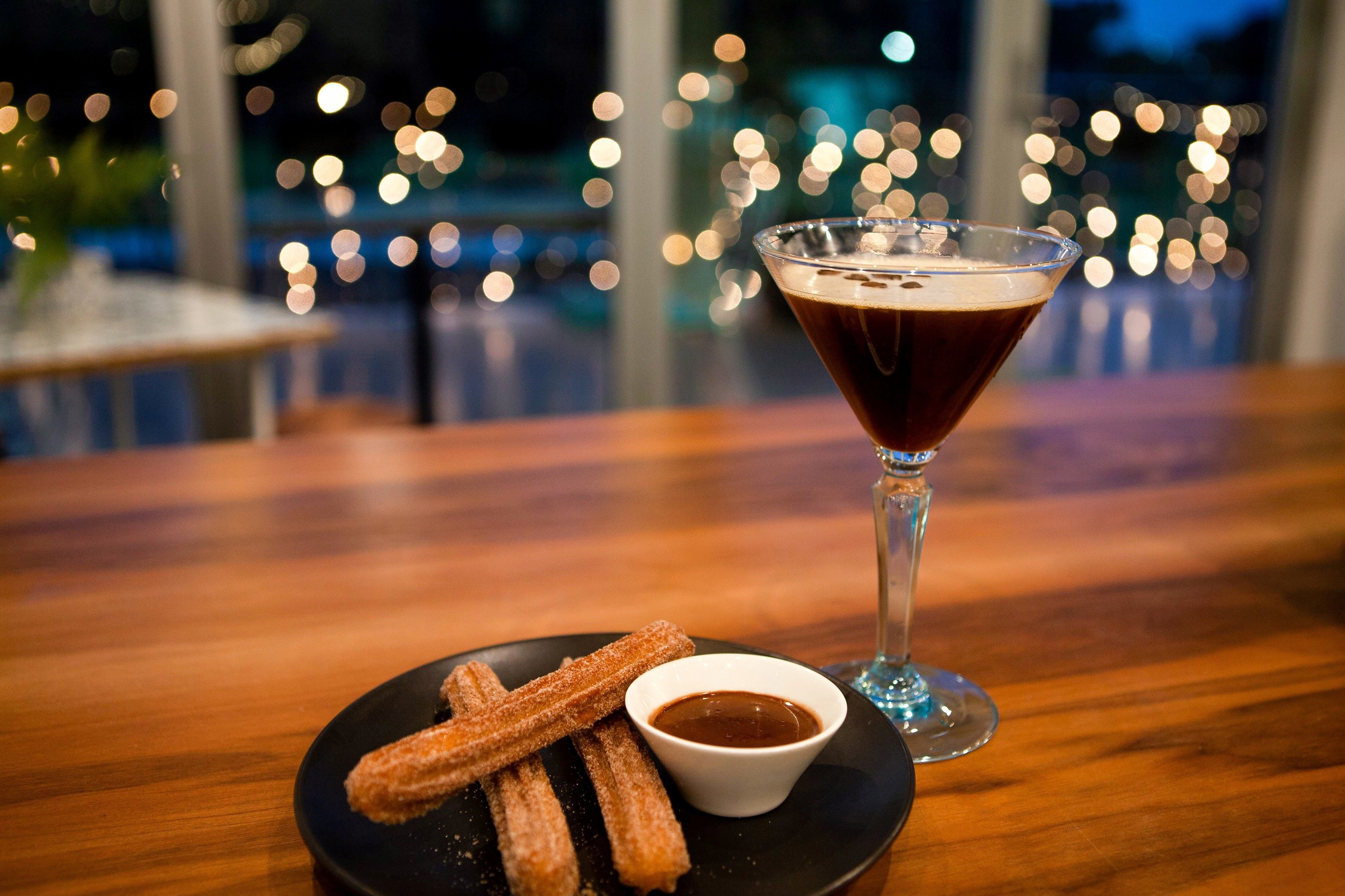 A plate of churros with a dipping sauce and a martini glass on a wooden table.