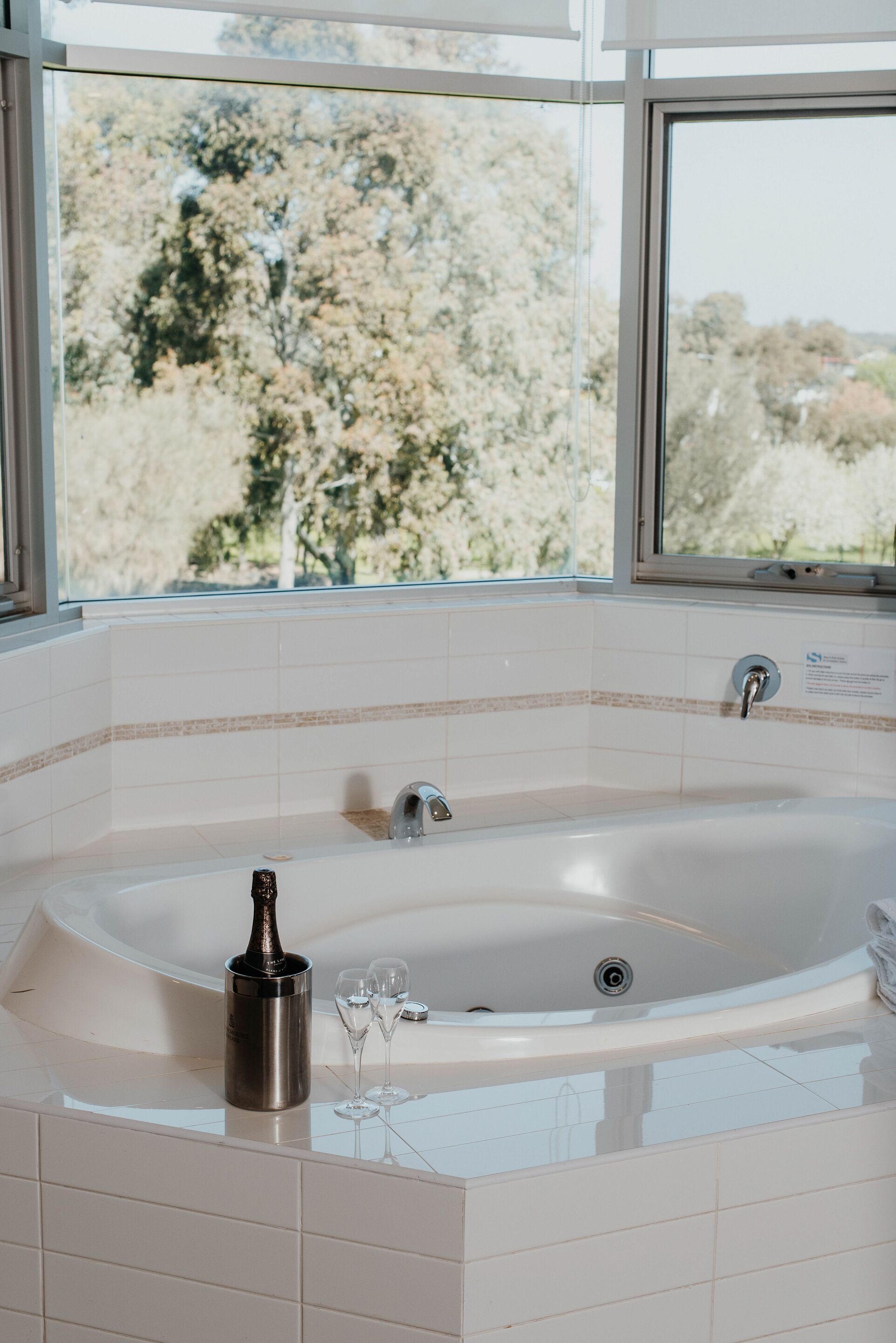 A modern bathroom with a large bathtub, a glass of champagne, and a bottle on the counter.