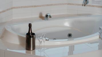 A modern bathroom with a large bathtub, a glass of champagne, and a bottle on the counter.