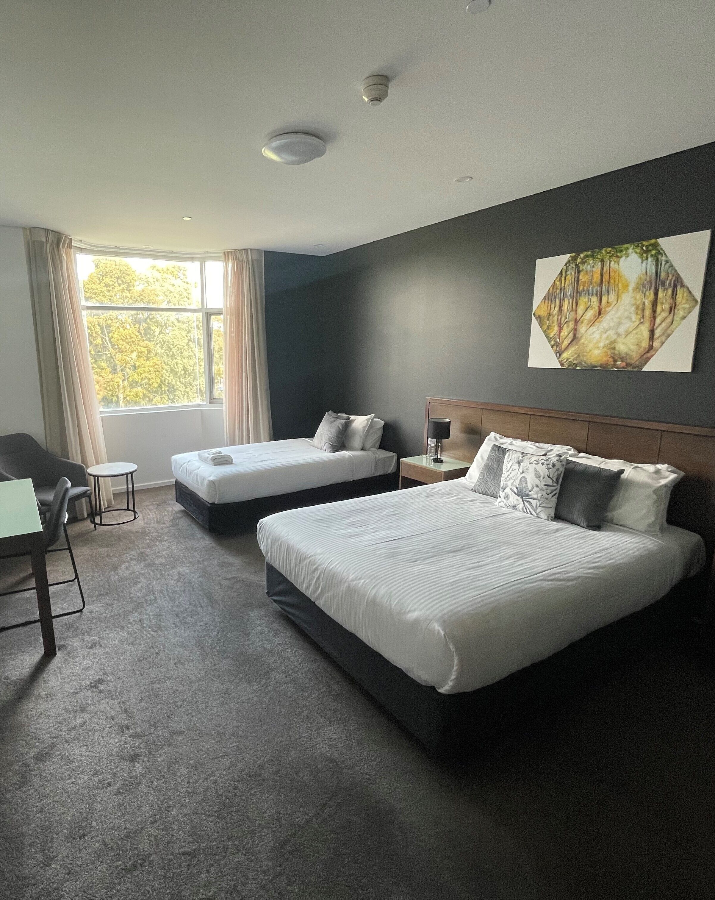 A hotel room with two beds, a desk, a chair, and a window with curtains.