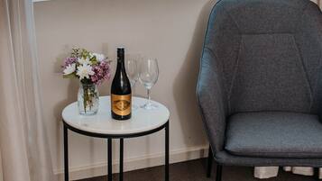 A room with a large window, a small round table with a bottle and glasses, and a grey chair.