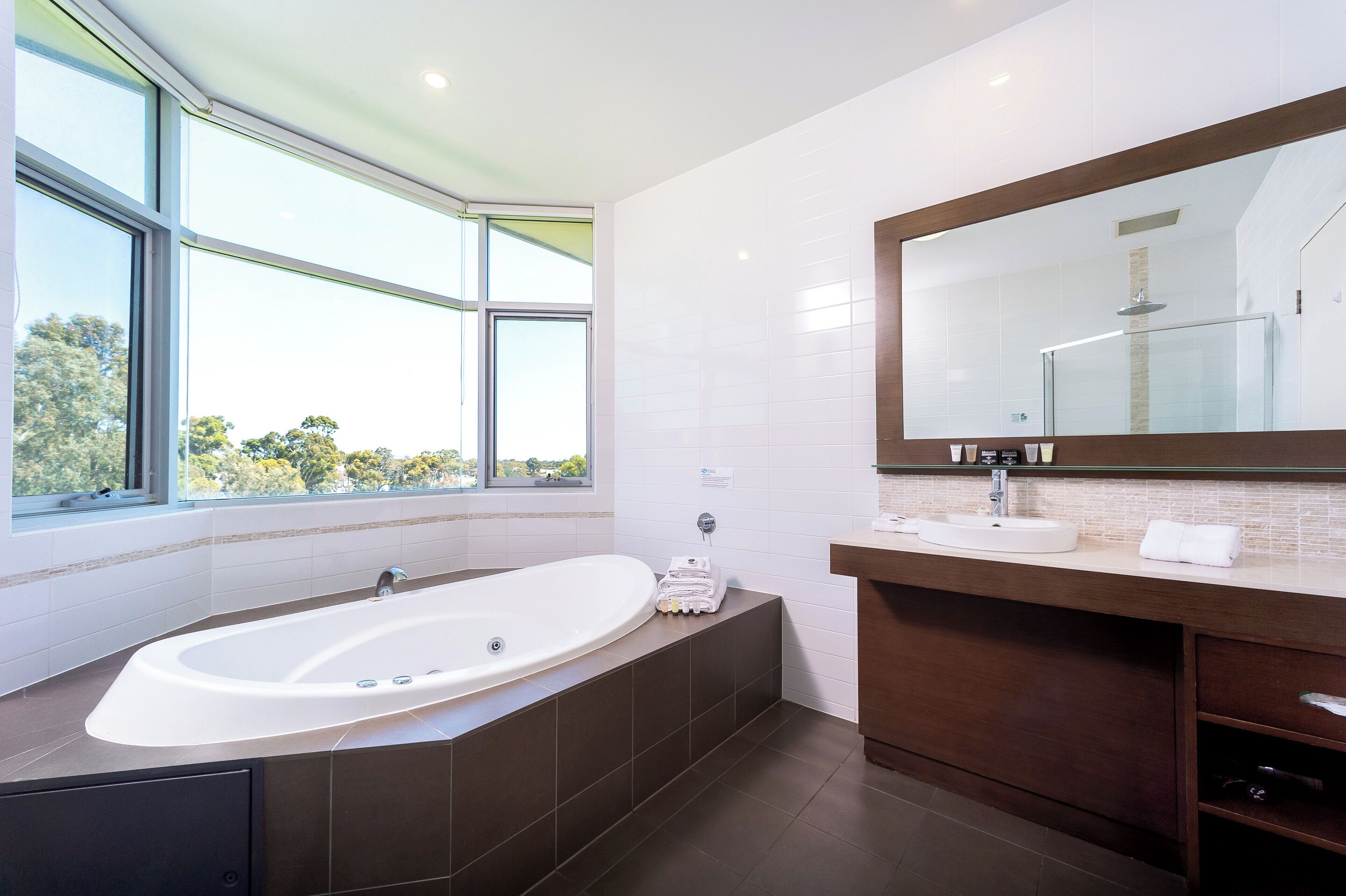 A modern bathroom with a large bathtub, a vanity with a mirror, and a window offering a view of trees.