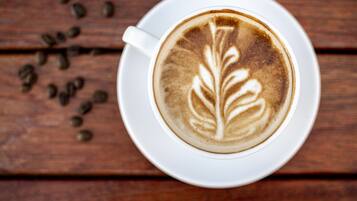 A cup of coffee with latte art on a white saucer, placed on a wooden surface with scattered coffee beans.