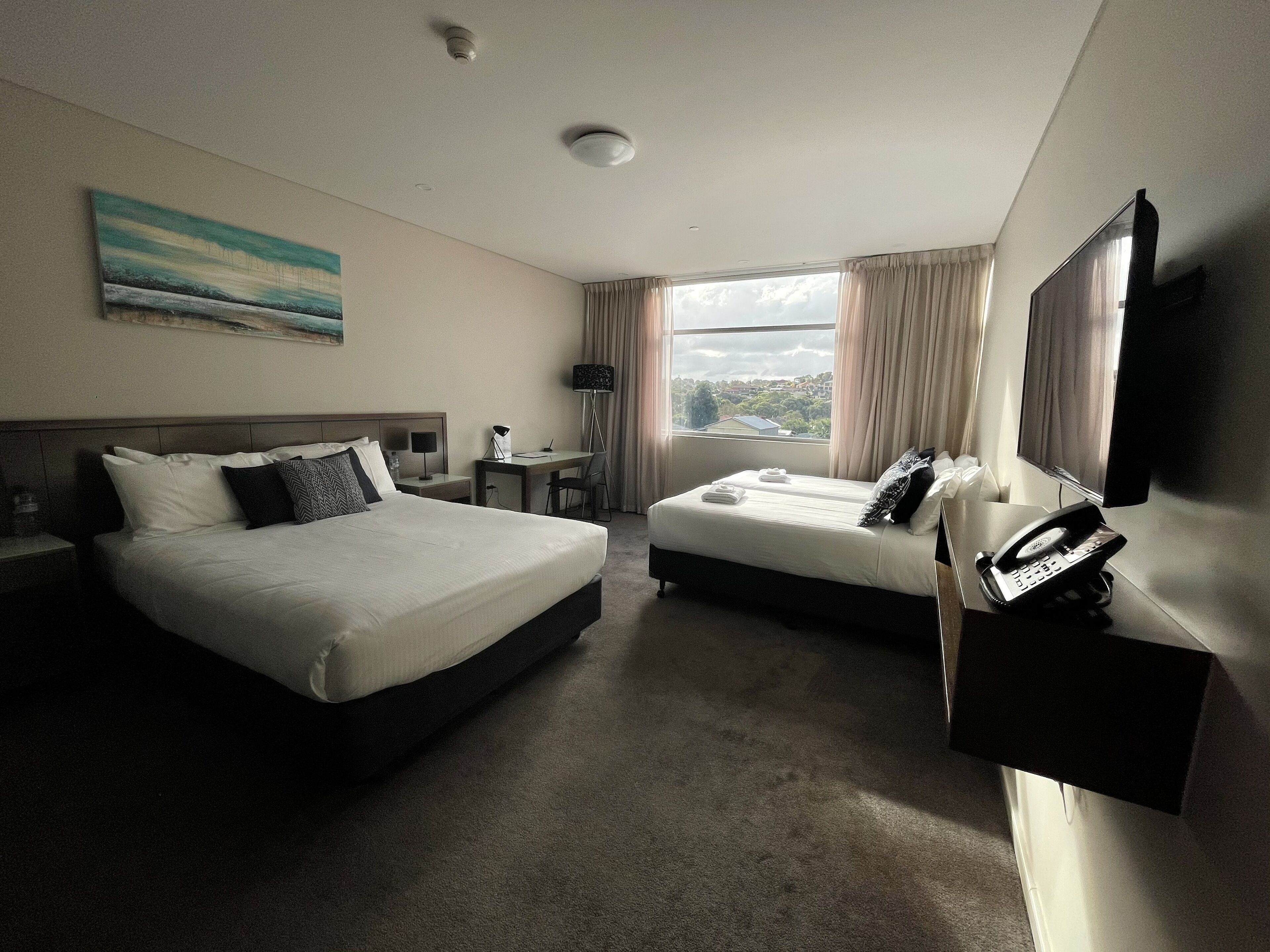 A hotel room with two beds, a desk, a chair, a flat-screen TV, and a telephone.
