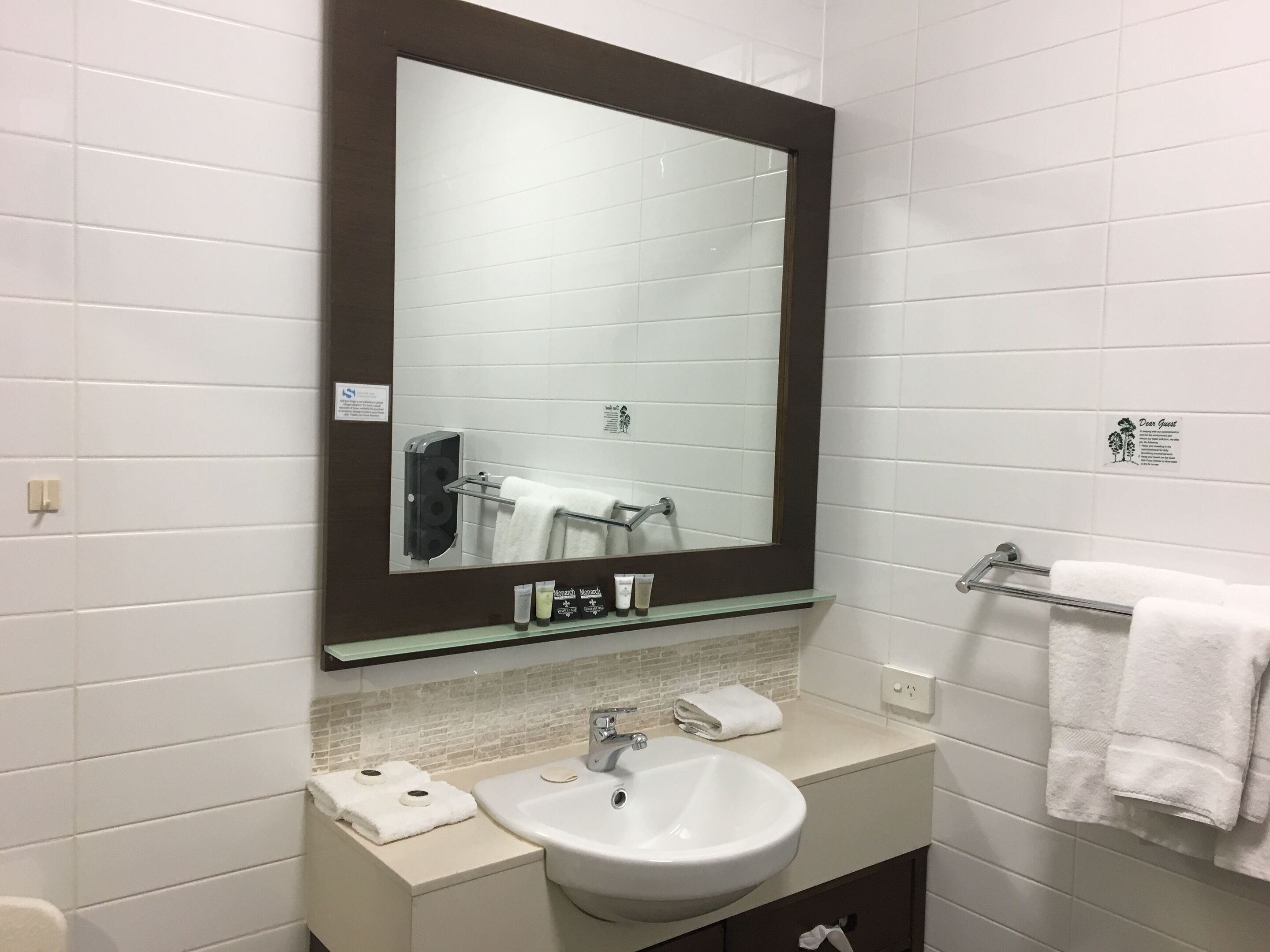 A bathroom with a large mirror, a sink, and a towel rack.