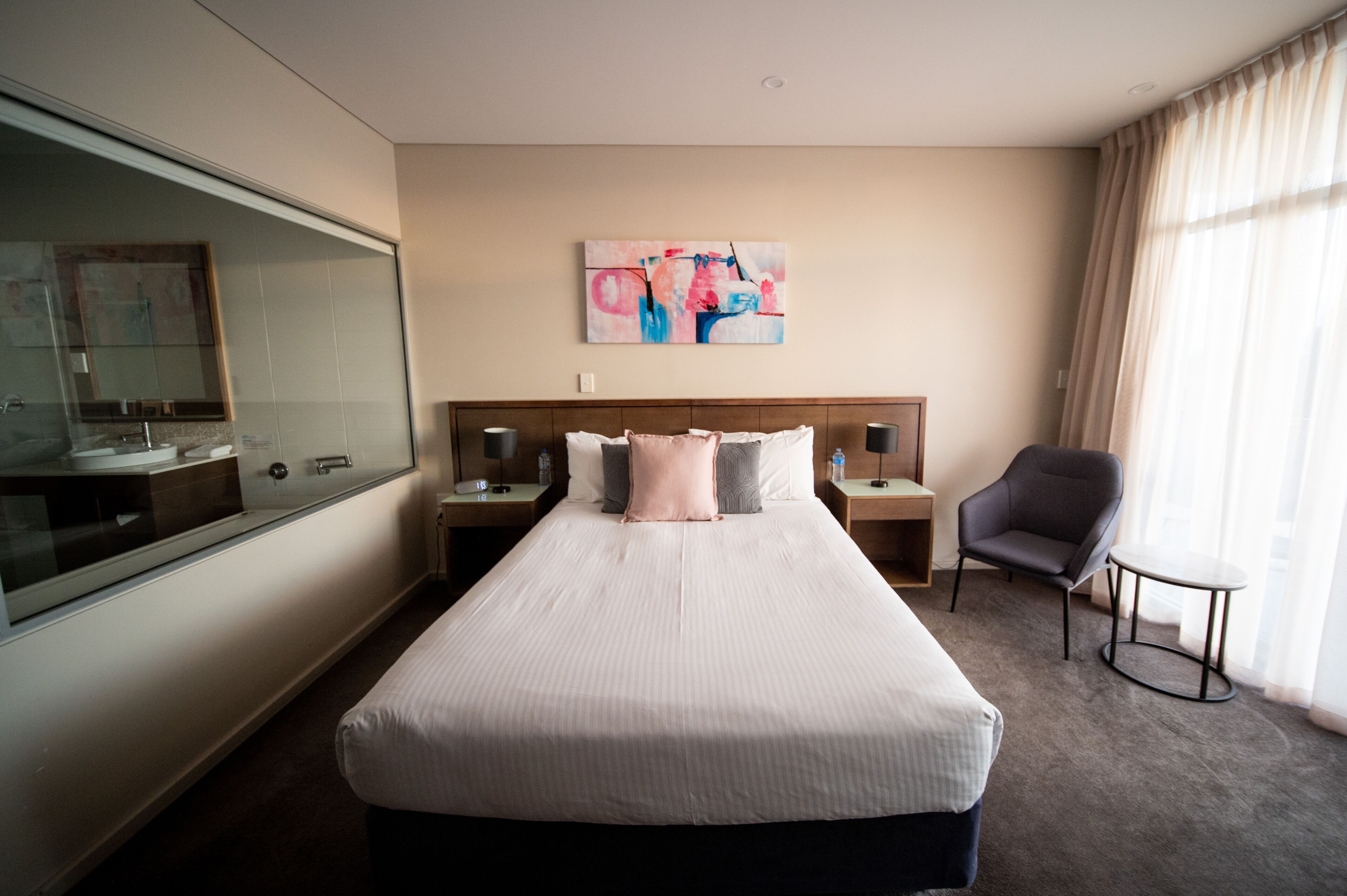 Una habitación de hotel con una cama grande, una mesita de noche con lámpara, una silla y una pequeña mesa.