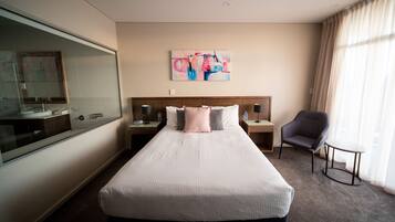 Una habitación de hotel con una cama grande, una mesita de noche con lámpara, una silla y una pequeña mesa.
