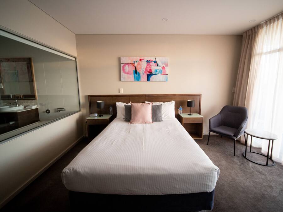 Una habitación de hotel con una cama grande, una mesita de noche con lámpara, una silla y una pequeña mesa.