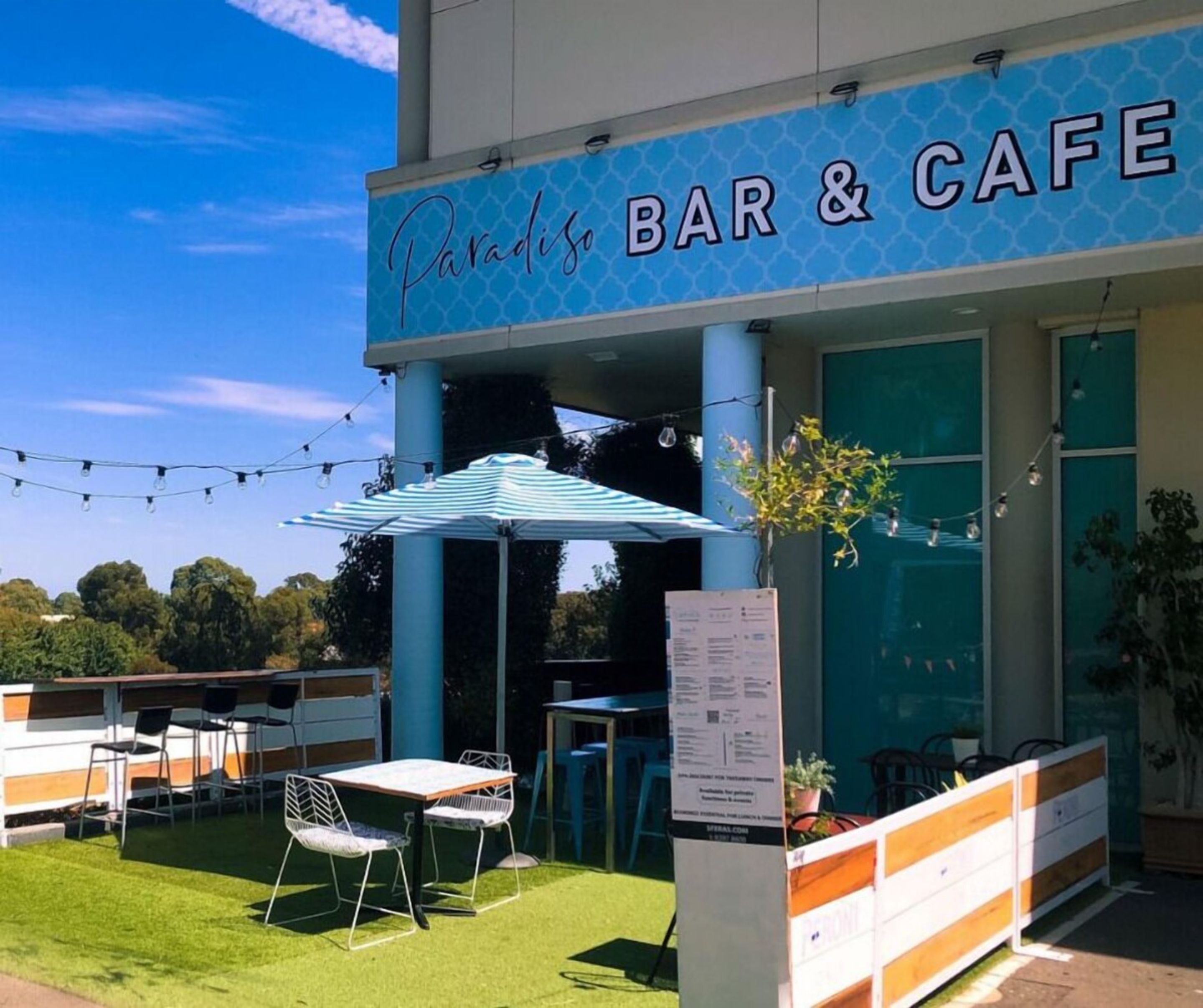 An outdoor seating area with tables and chairs, a sign reading "Paradiso BAR & CAFE", and a menu board.