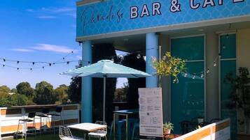 An outdoor seating area with tables and chairs, a sign reading "Paradiso BAR & CAFE", and a menu board.