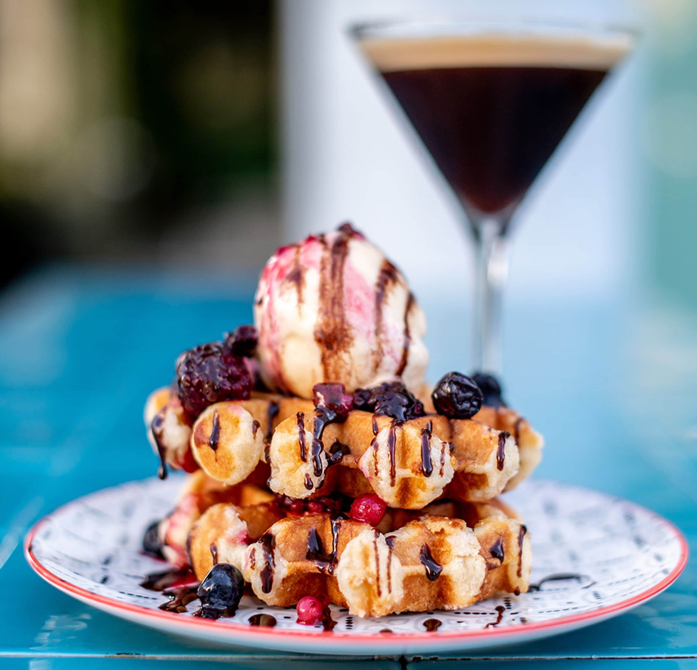 A plate of waffles topped with berries and syrup, with a martini glass in the background.