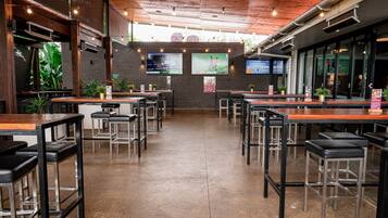 A restaurant with multiple tables and chairs, a brick wall, and two large screens displaying sports.