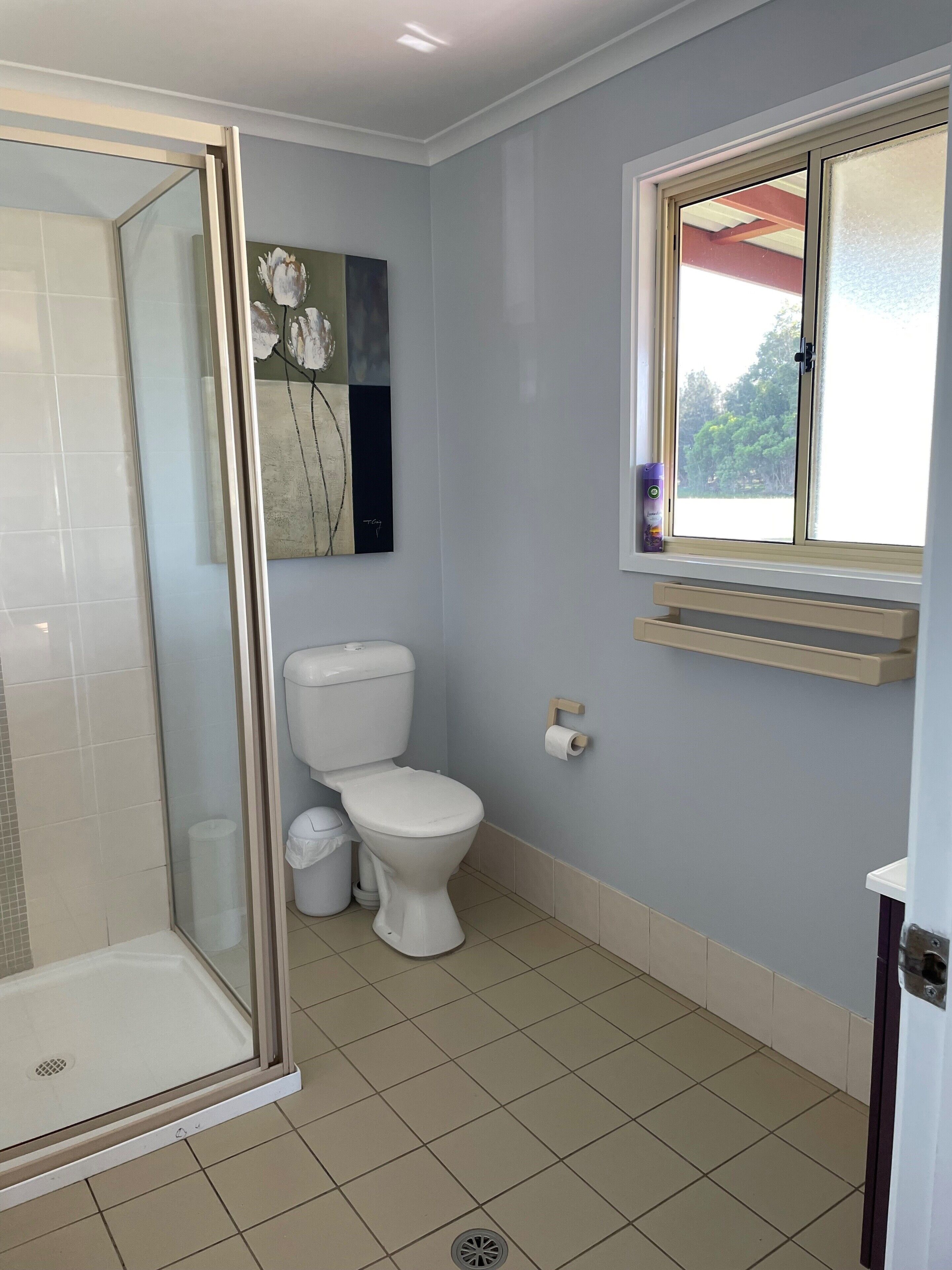 Ein Badezimmer mit Dusche, Toilette und einem Fenster mit Blick auf Bäume.