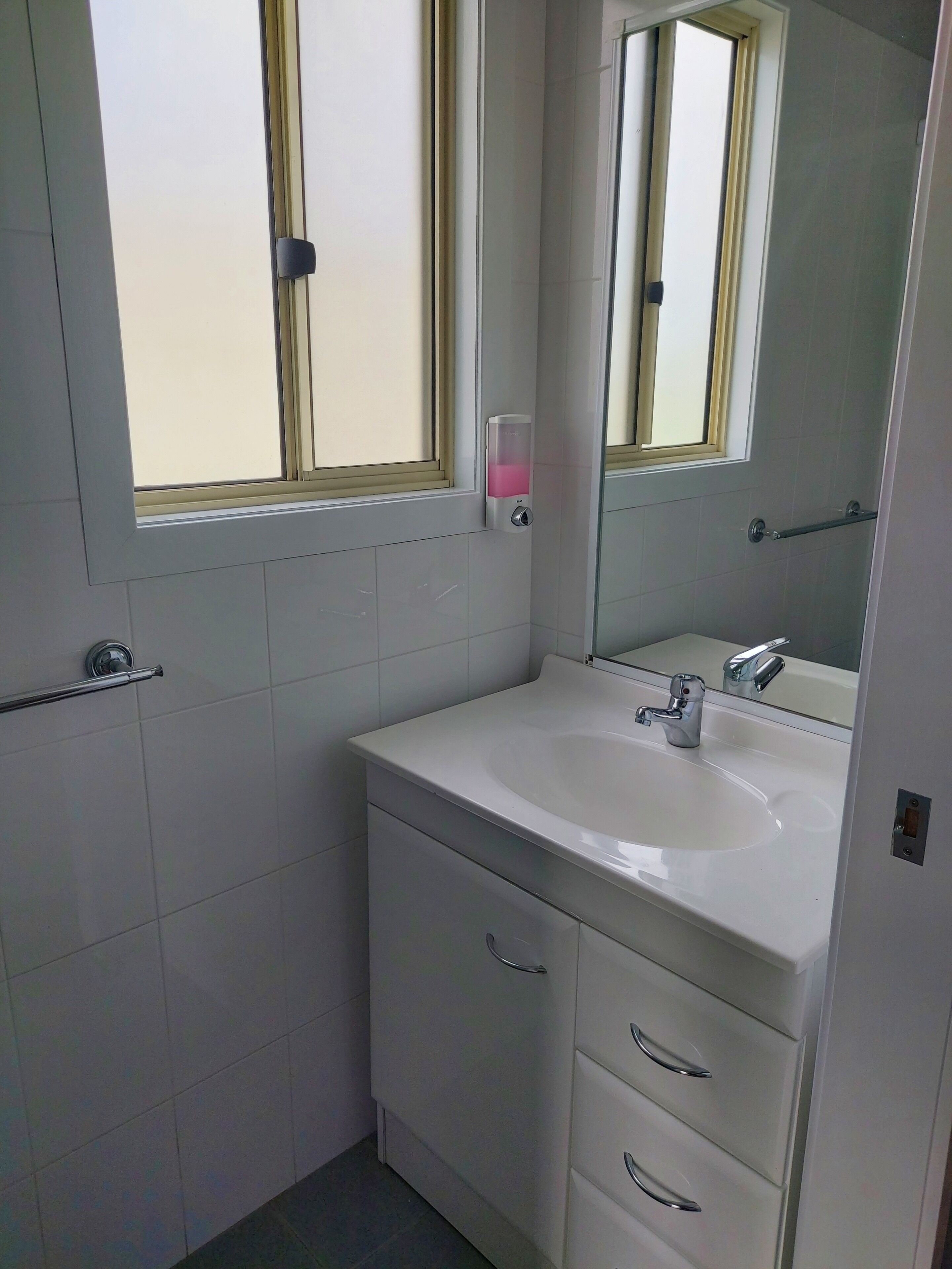 A bathroom with a white sink, a mirror, and a window with a frosted glass panel.