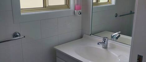 A bathroom with a white sink, a mirror, and a window with a frosted glass panel.