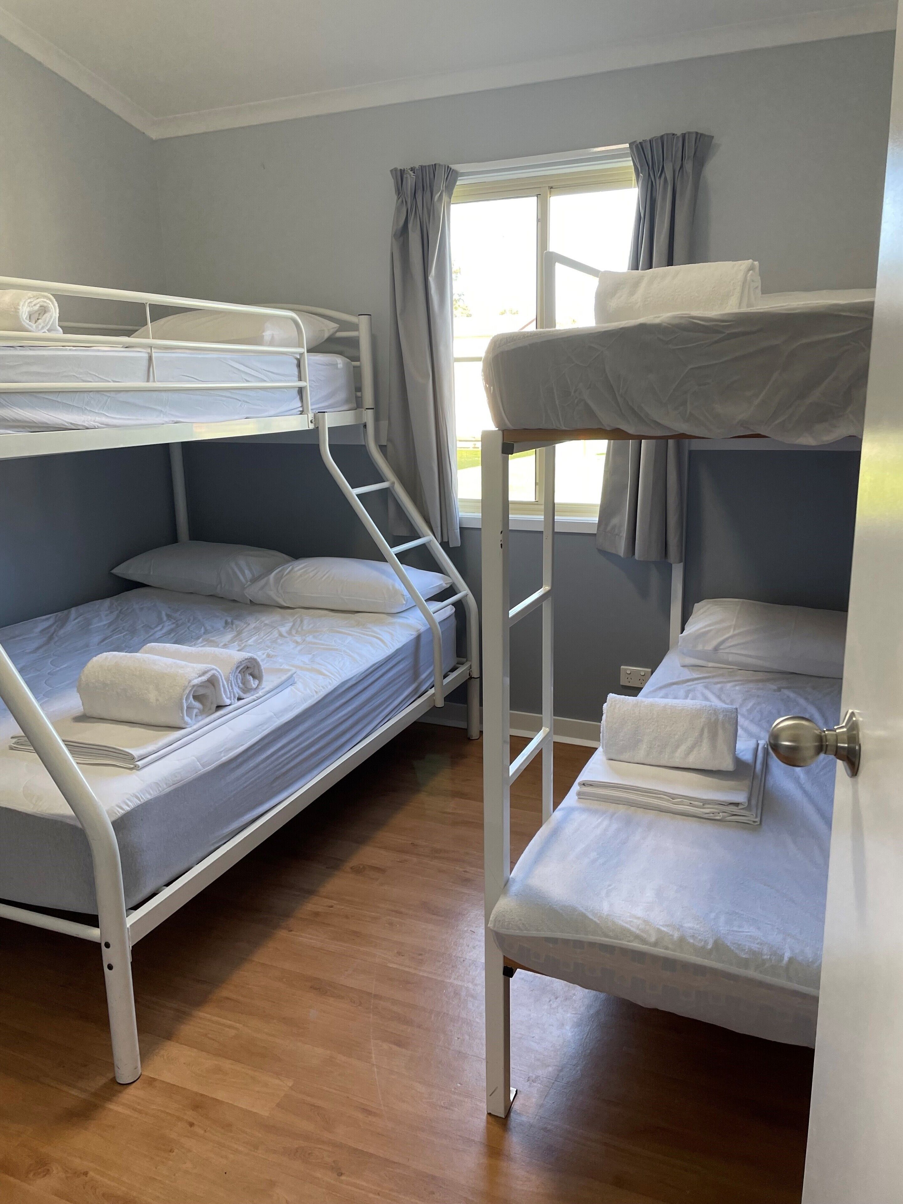 Une chambre de dortoir avec des lits superposés, une fenêtre avec des rideaux et un plancher en bois.