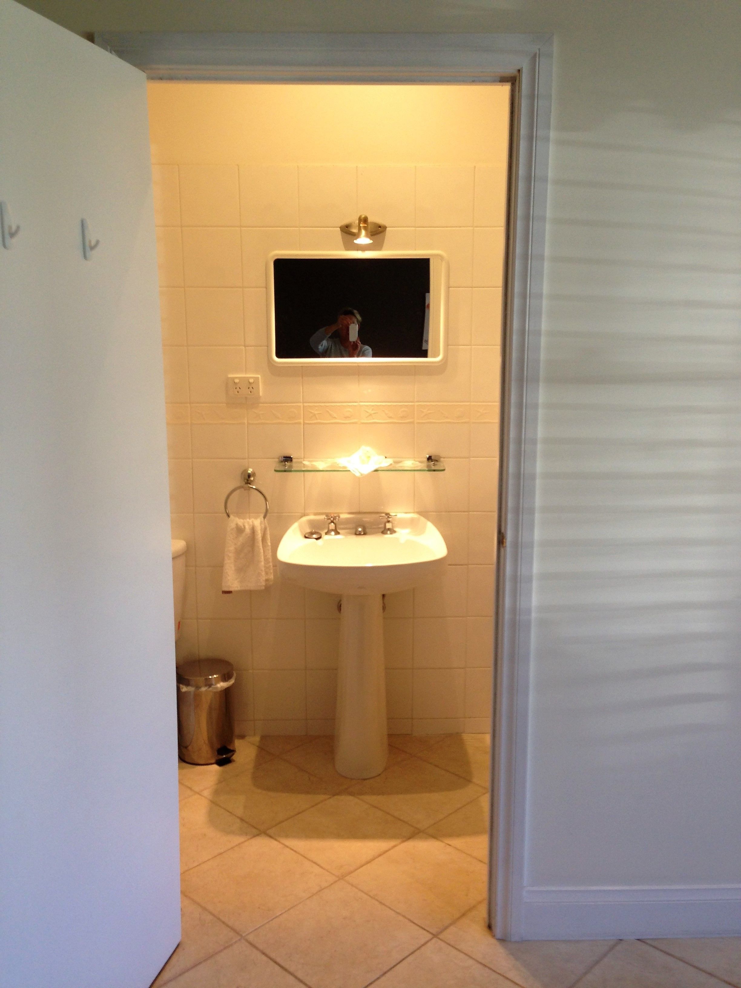 A bathroom with a white sink, a mirror above it, and a trash can.
