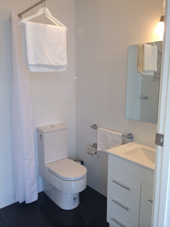 A modern bathroom with a toilet, a sink, and a mirror. - Ruby's Queenscliff (Queenscliff)