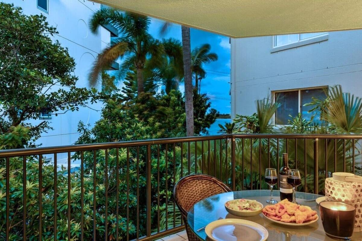 A balcony with a table set for dining, surrounded by lush greenery and palm trees.