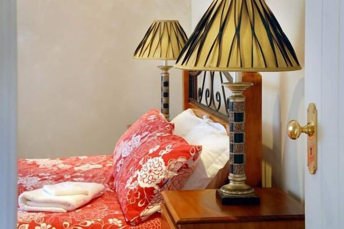 Ein Bett mit einer rot-weißen Bettdecke, zwei Lampen mit gestreiften Lampenschirmen und ein Nachttisch aus Holz.