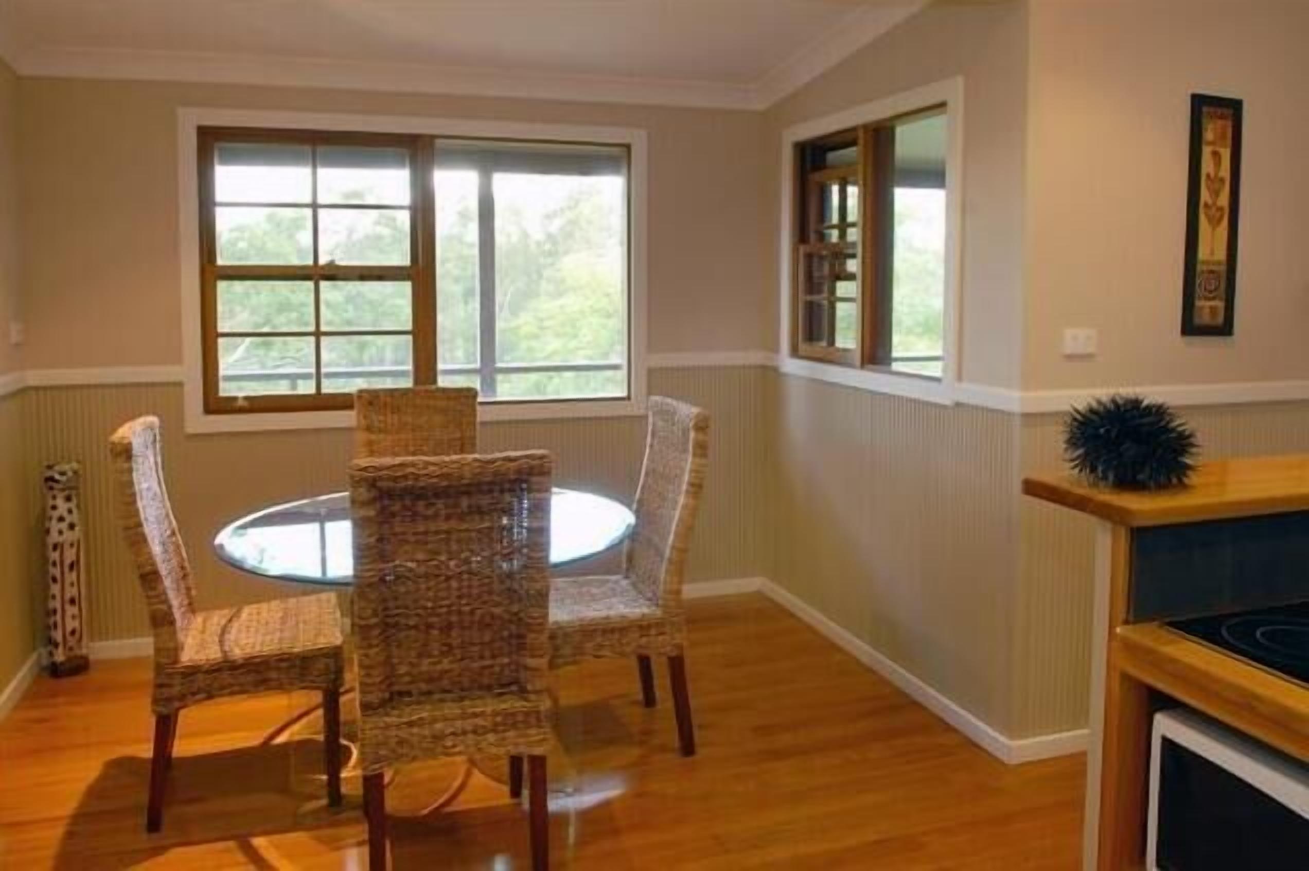 A dining area with a round table and four wicker chairs, large windows with blinds, and a fireplace with a decorative plant.