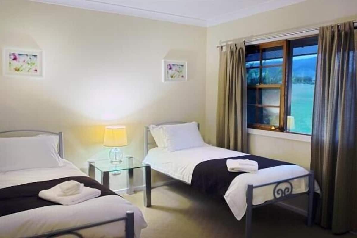 Ein Hotelzimmer mit zwei Einzelbetten, einem Nachttisch mit Lampe und einem Fenster mit Vorhängen.