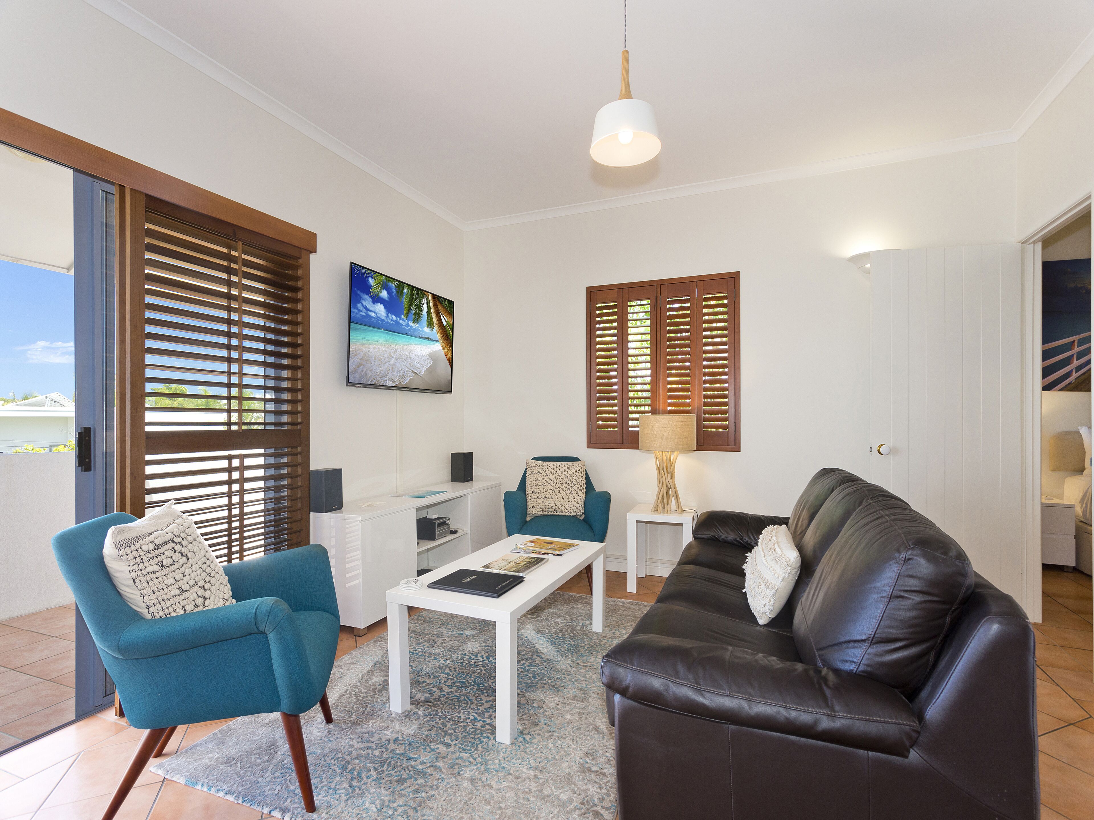 A living room with a blue armchair, a brown leather sofa, a coffee table, a TV, and a lamp.