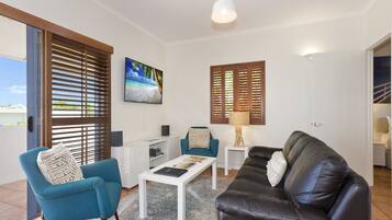 A living room with a blue armchair, a brown leather sofa, a coffee table, a TV, and a lamp.