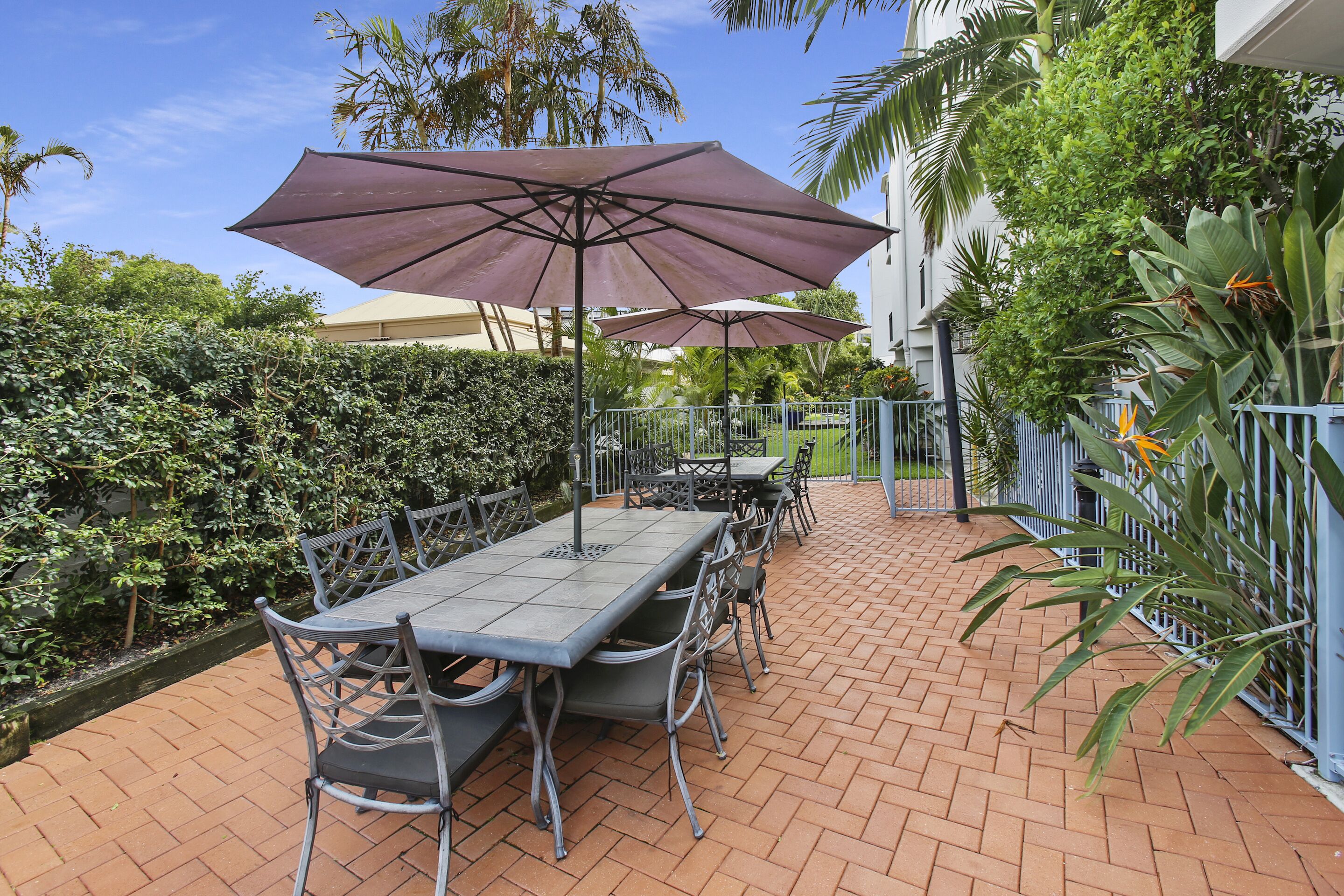Une terrasse extérieure avec une table et des chaises, entourée d’un sol en briques et de rampes en métal.