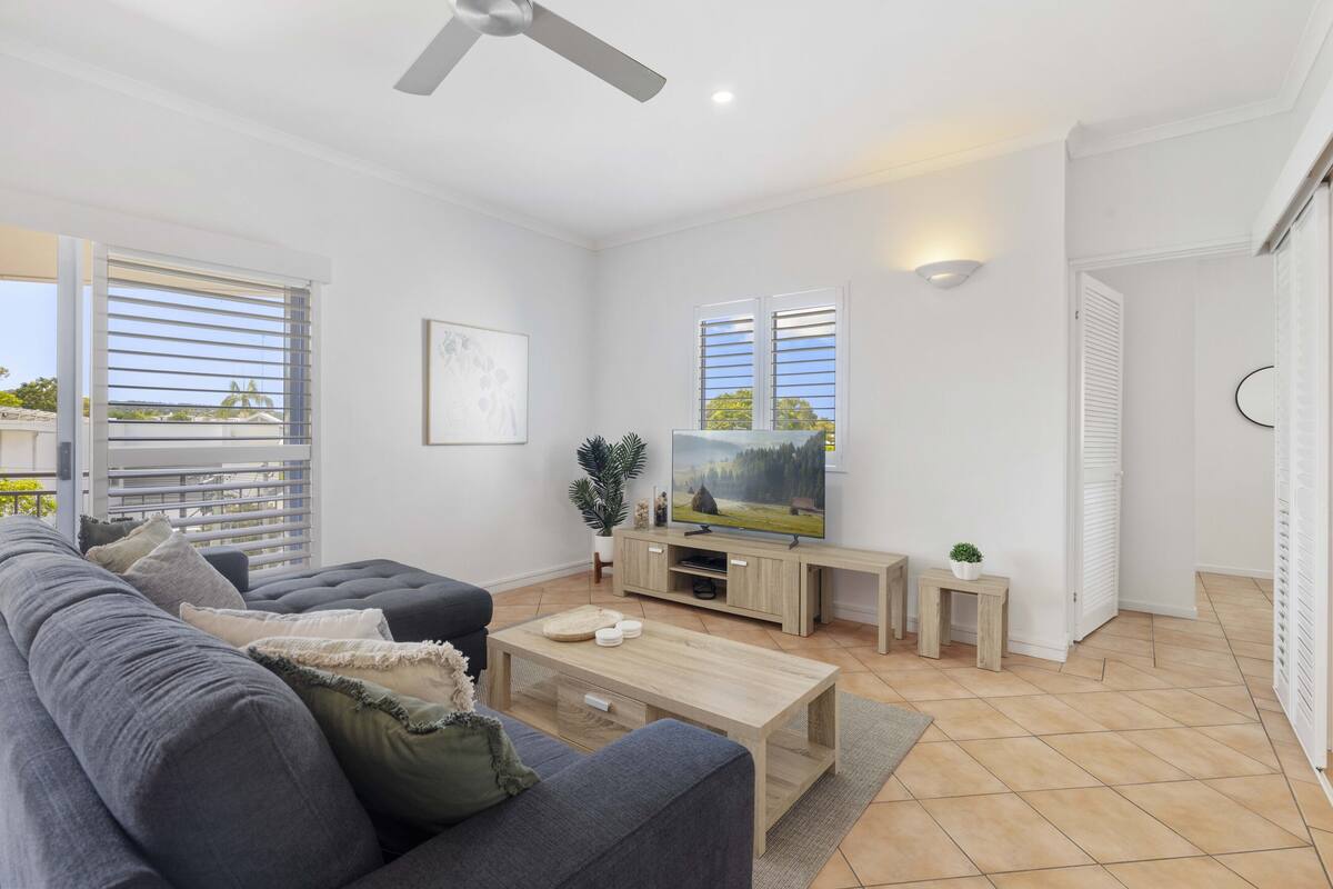 A modern living room with a grey sofa, wooden coffee table, and a TV on a wooden stand.