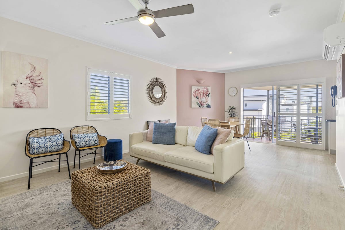 A living room with a beige sofa, two wicker chairs, a coffee table, and a ceiling fan.