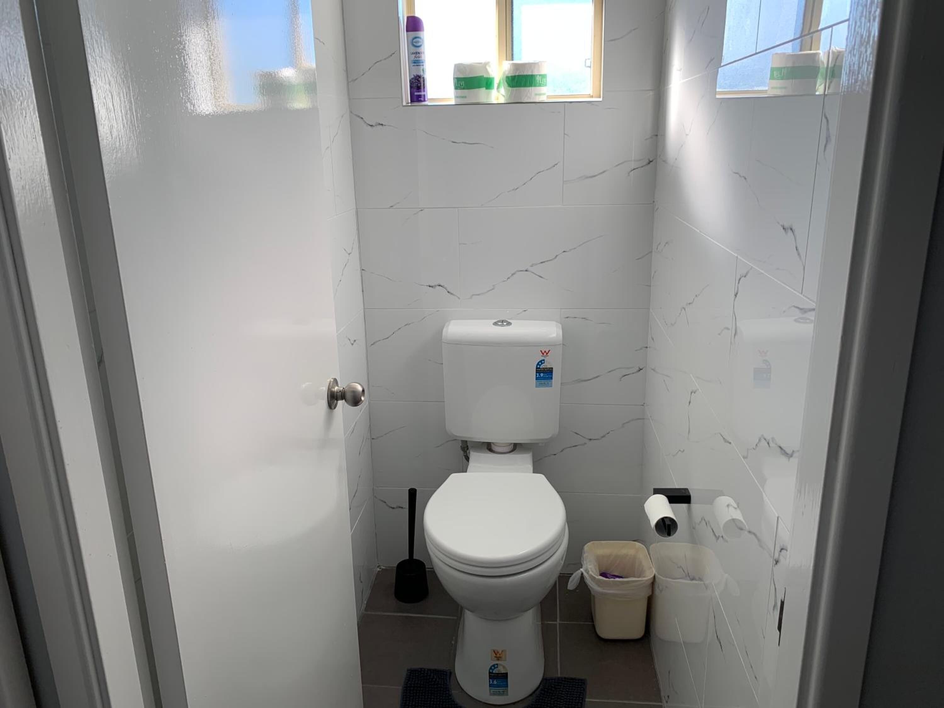 A small bathroom with a toilet, a bidet, a trash bin, and a window.
