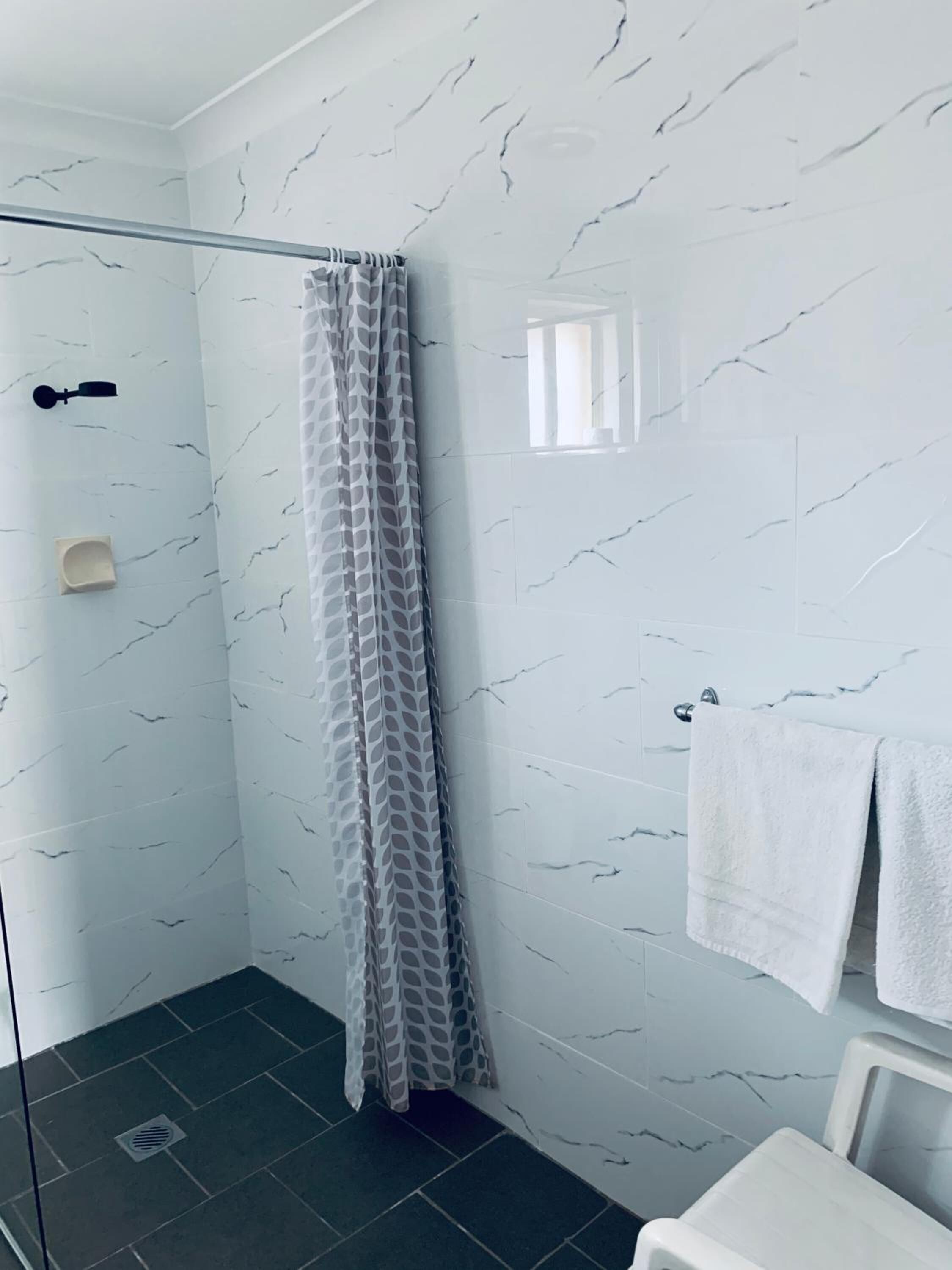 Une salle de bain moderne avec une douche à parois de verre, des murs en marbre blanc et un lavabo blanc, avec une serviette accrochée au mur.