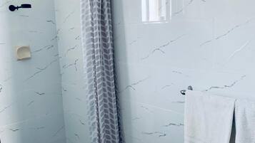 Une salle de bain moderne avec une douche à parois de verre, des murs en marbre blanc et un lavabo blanc, avec une serviette accrochée au mur.