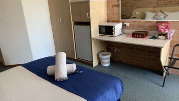 A hotel room with a bed, a desk with a microwave, a tea station, and a trash bin.