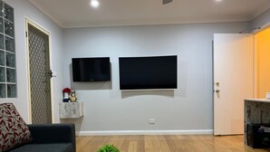 A living room with a sofa, two mounted TVs, a small plant on a table, and a door. - Branxton House Motel, Hunter Valley (Branxton)