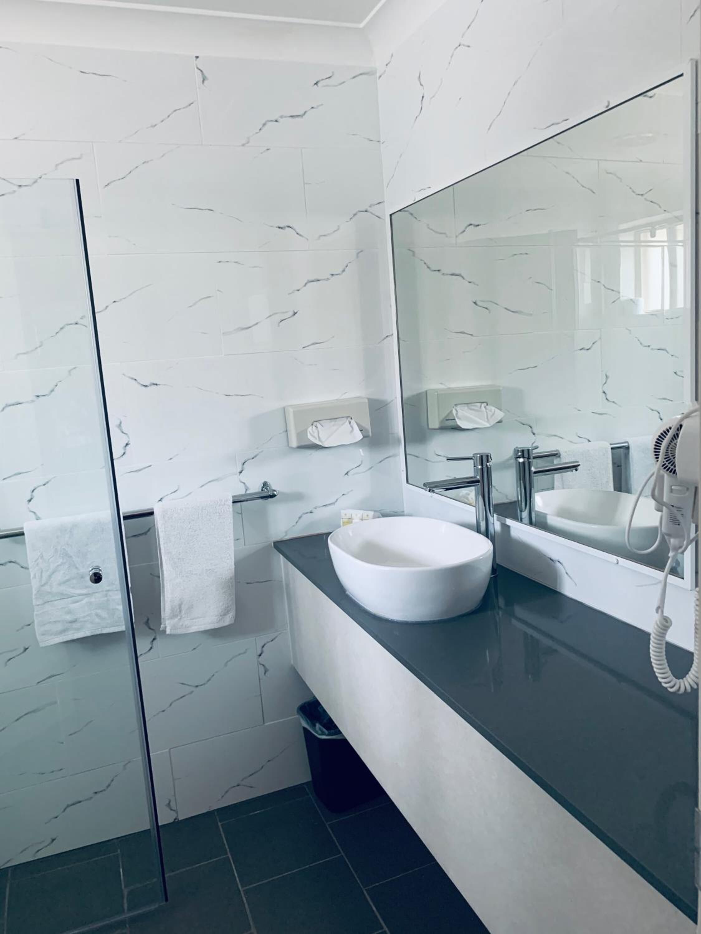Un baño moderno con una salpicadura de mármol blanco, un espejo grande, un lavabo blanco y un secador de pelo en la encimera.