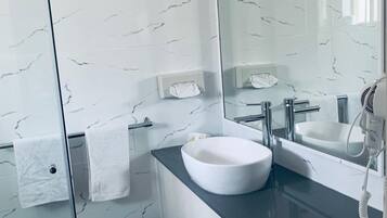 Un baño moderno con una salpicadura de mármol blanco, un espejo grande, un lavabo blanco y un secador de pelo en la encimera.