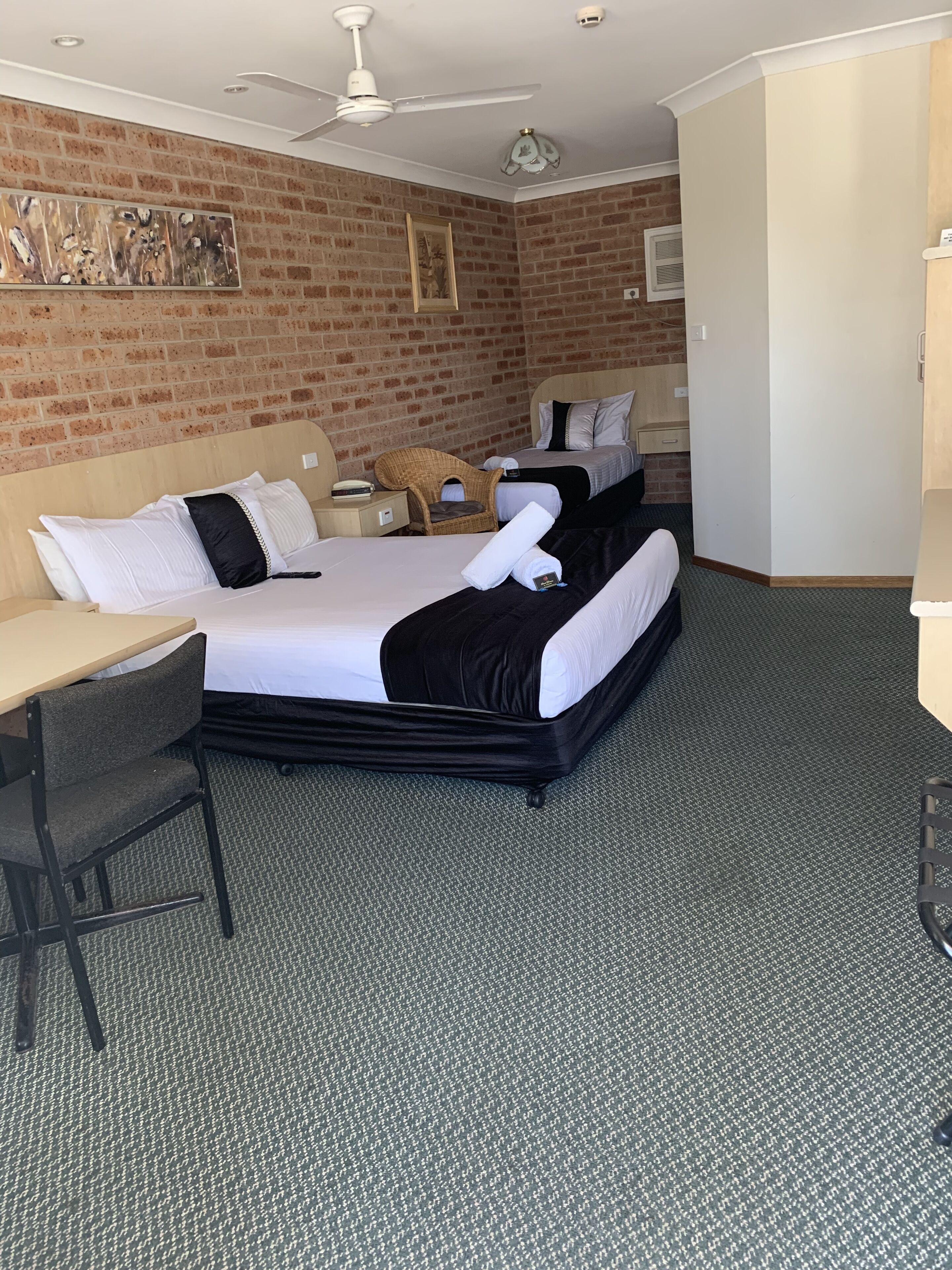 Habitación de hotel con una cama grande, un escritorio, una silla, un armario y un ventilador de techo.