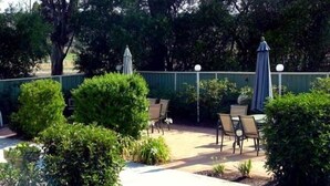 An outdoor patio area with chairs and a table, surrounded by greenery and a fence. - Branxton House Motel, Hunter Valley (Branxton)