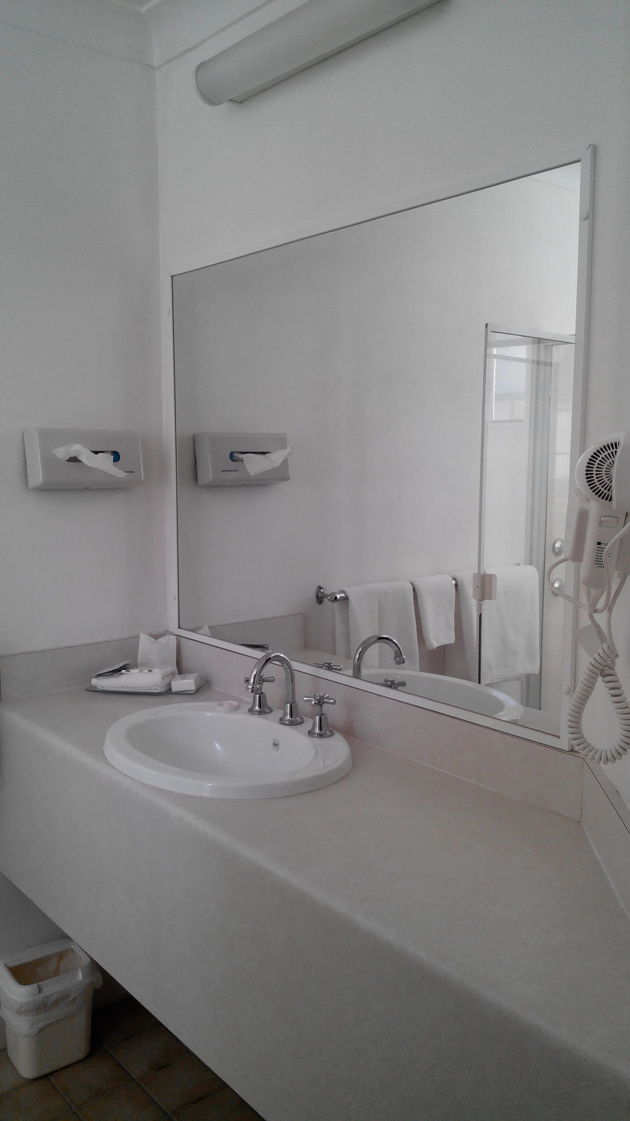Un baño moderno con un lavamanos blanco, dos grifos, un espejo grande y un secador de pelo sobre la encimera.