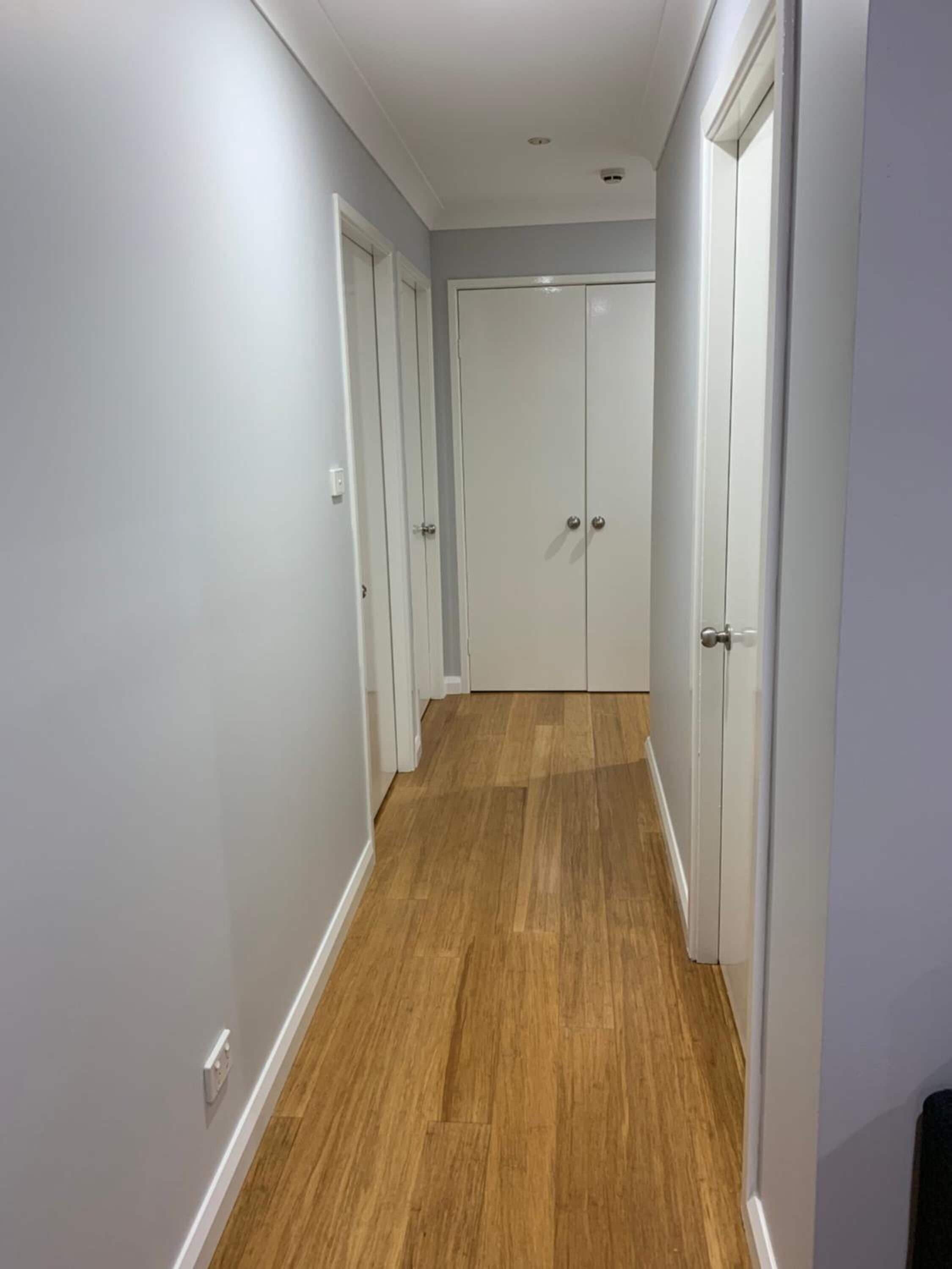 A narrow hallway with wooden flooring and white walls.