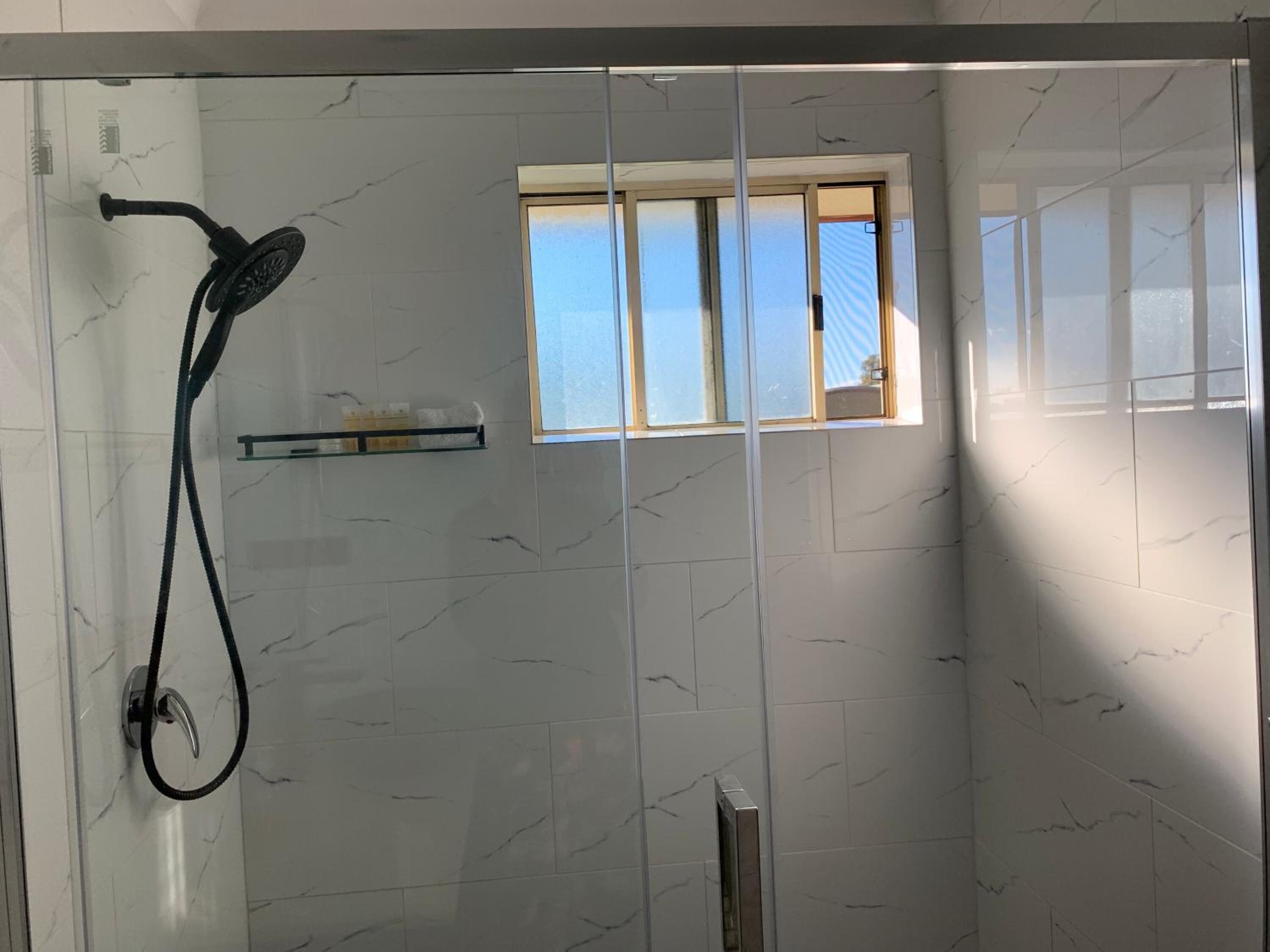 A shower area with a glass door, a handheld showerhead, and a window.