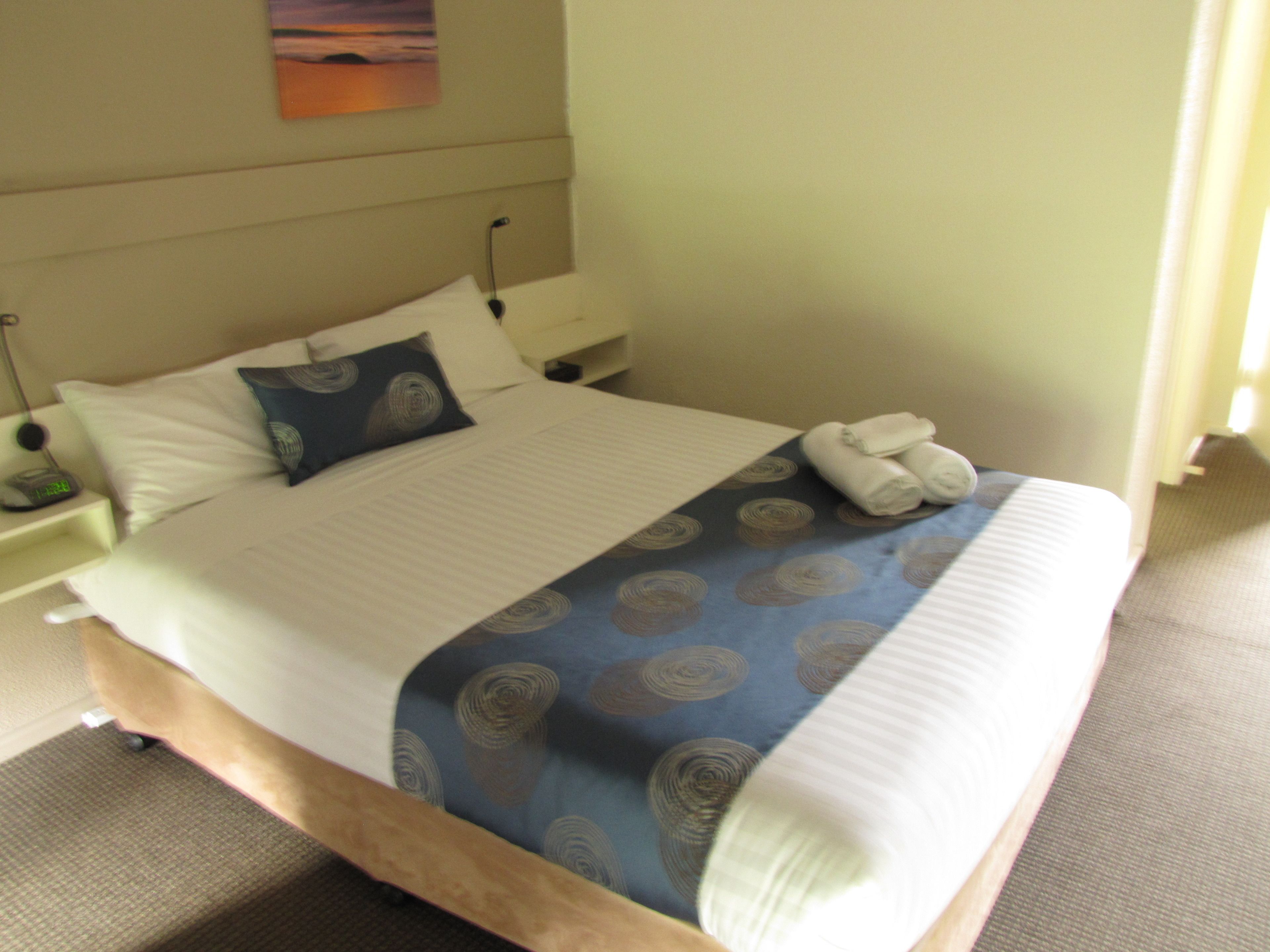 A neatly made bed with a blue patterned bedspread, white pillows, and a folded towel on the side.