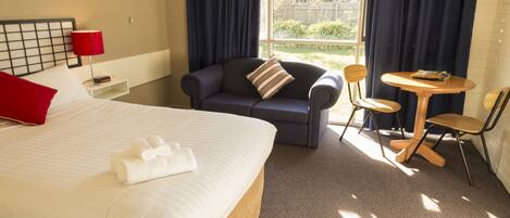 A hotel room with a large bed, a sofa, a small table, and a chair.