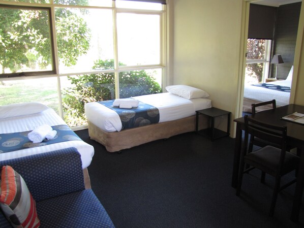 A hotel room with two beds, a small table, a chair, and a view of the outdoors.