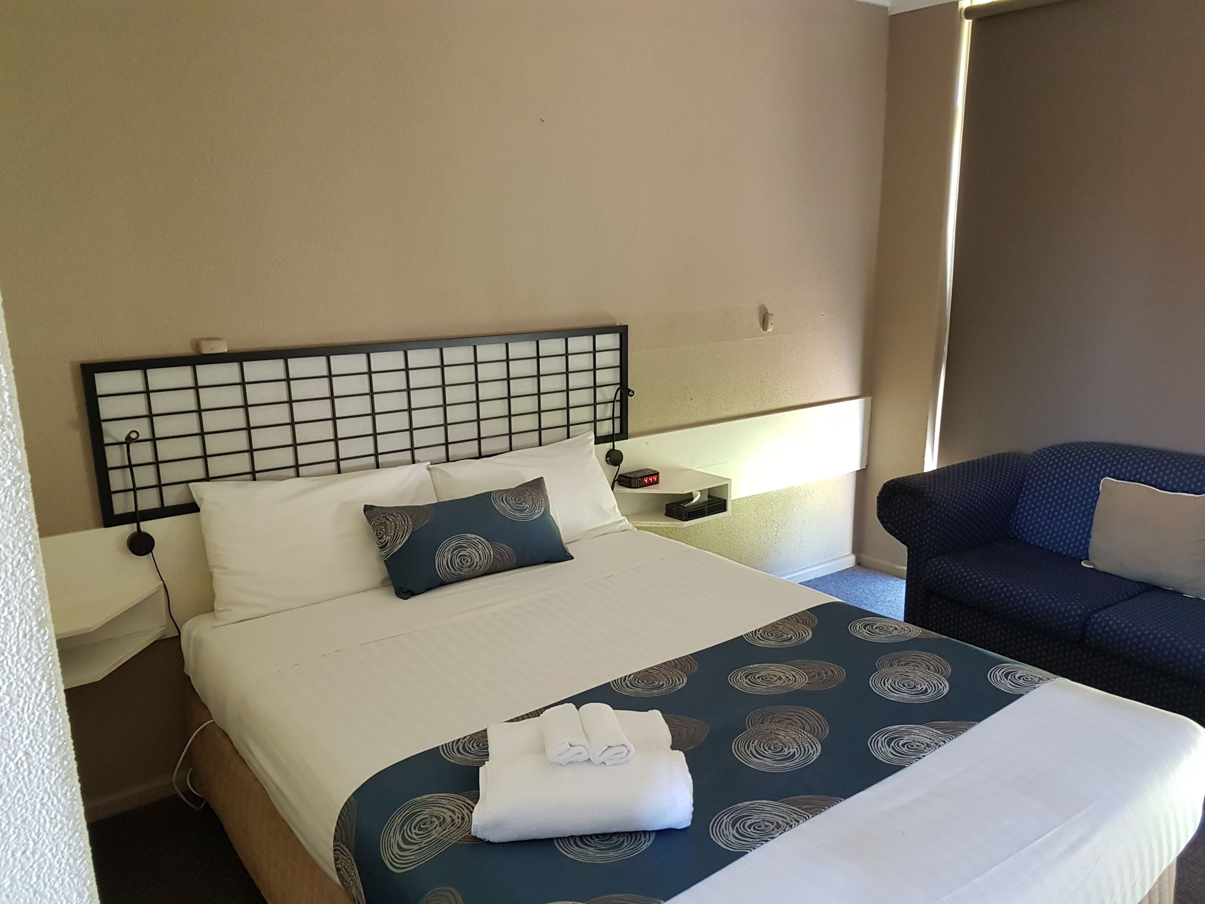 A hotel room with a bed, a nightstand, a lamp, a chair, and a window.