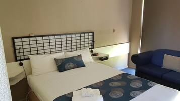 A hotel room with a bed, a nightstand, a lamp, a chair, and a window.