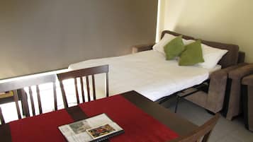 A small, neatly arranged room with a single bed, a table with a red table runner, and two chairs.